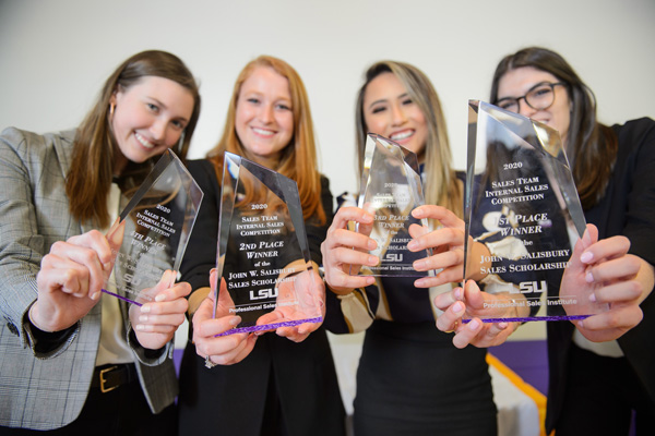 Female students hold up trophies from competition win. 