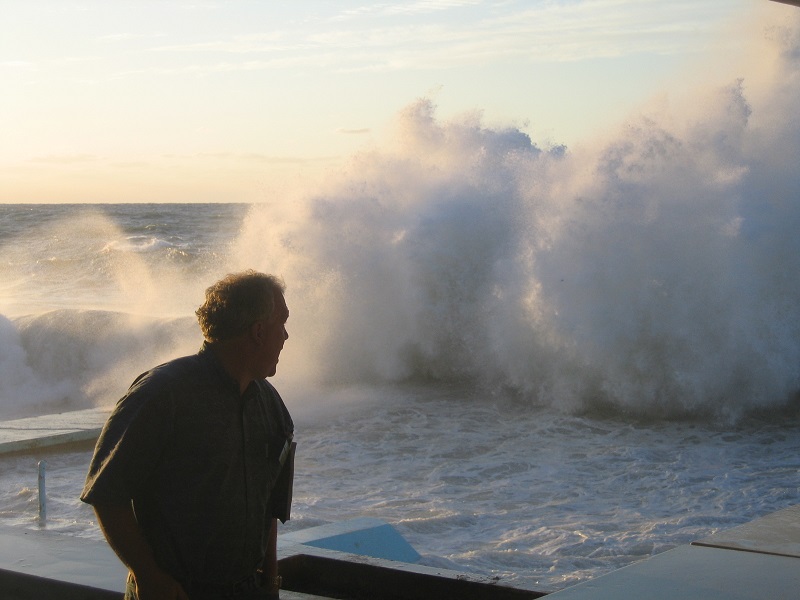 a man watches as a wave creates an ocean spray