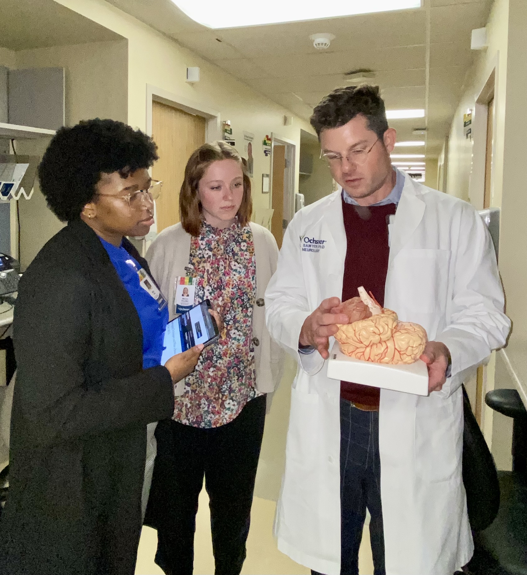African American female and White female holding clipboard and tablet and taking with a white male doctor holding model of the human brain