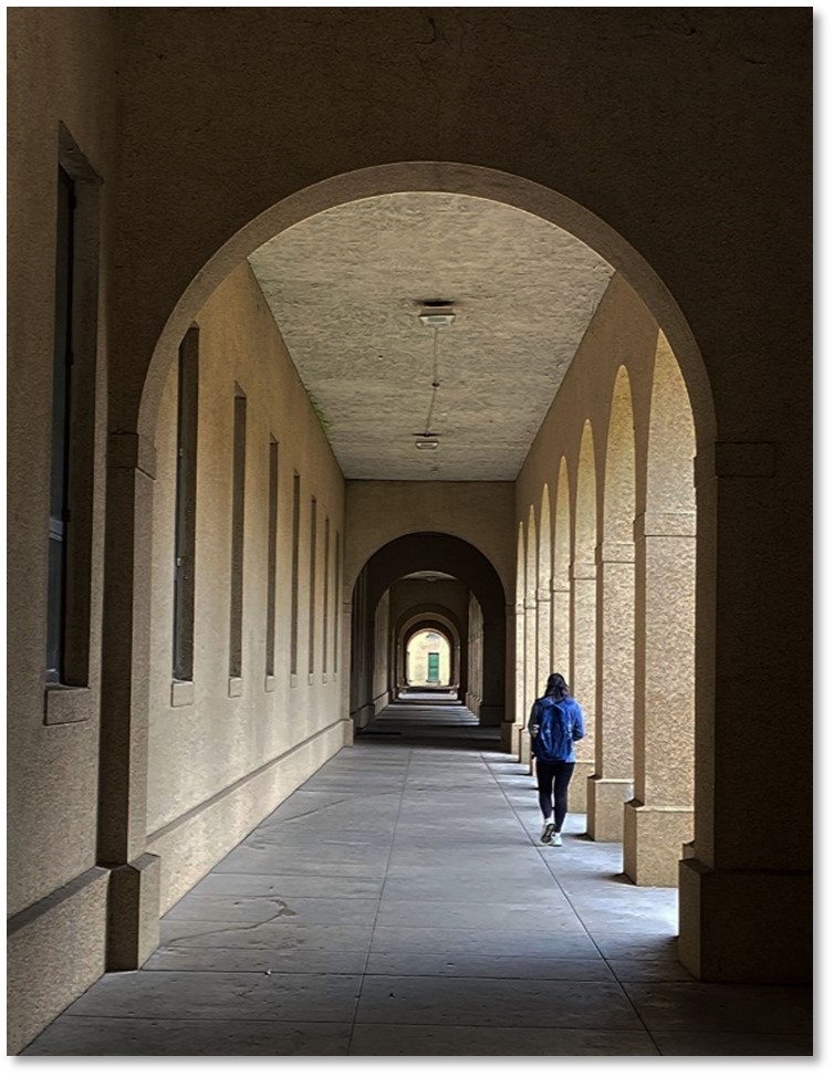 stone arched walkways near academic buildin entryways opened up to the LSU Quad with student in blue walking in the right side of the frame