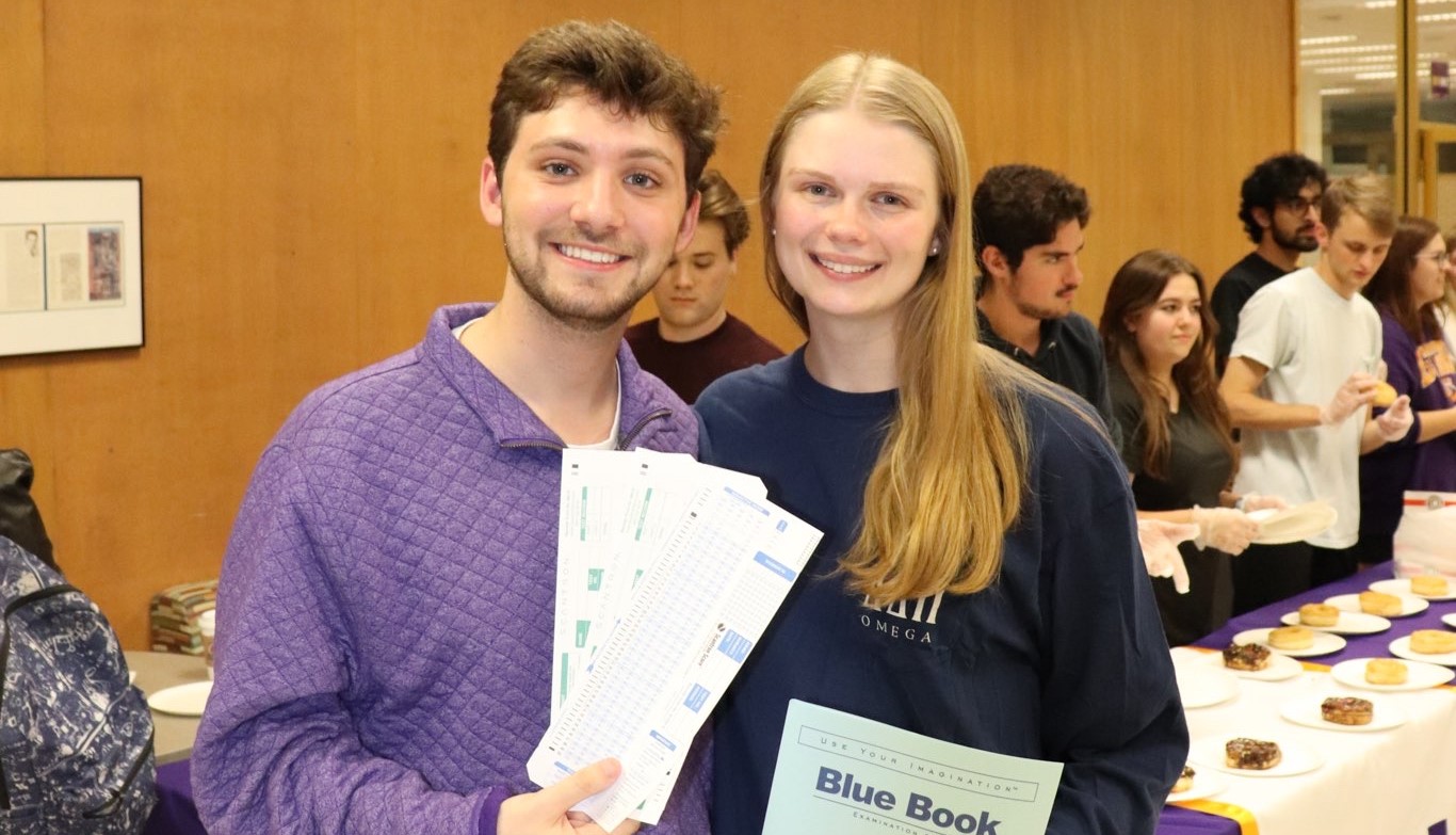 matthew and emma smile whil holding scantrons and a blue book