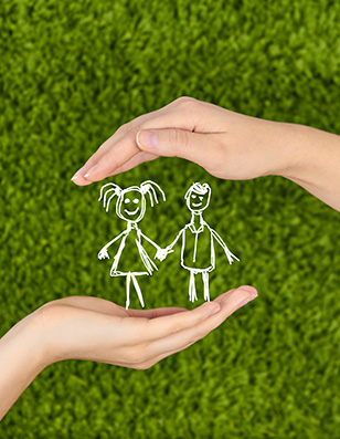 White child's drawing of a boy and girl held between two hands over a green grass background.